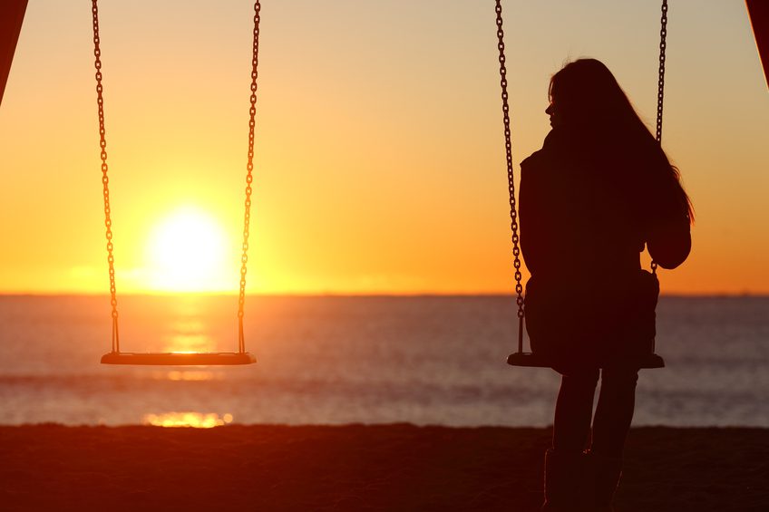 Single woman alone swinging on the beach and looking the other seat