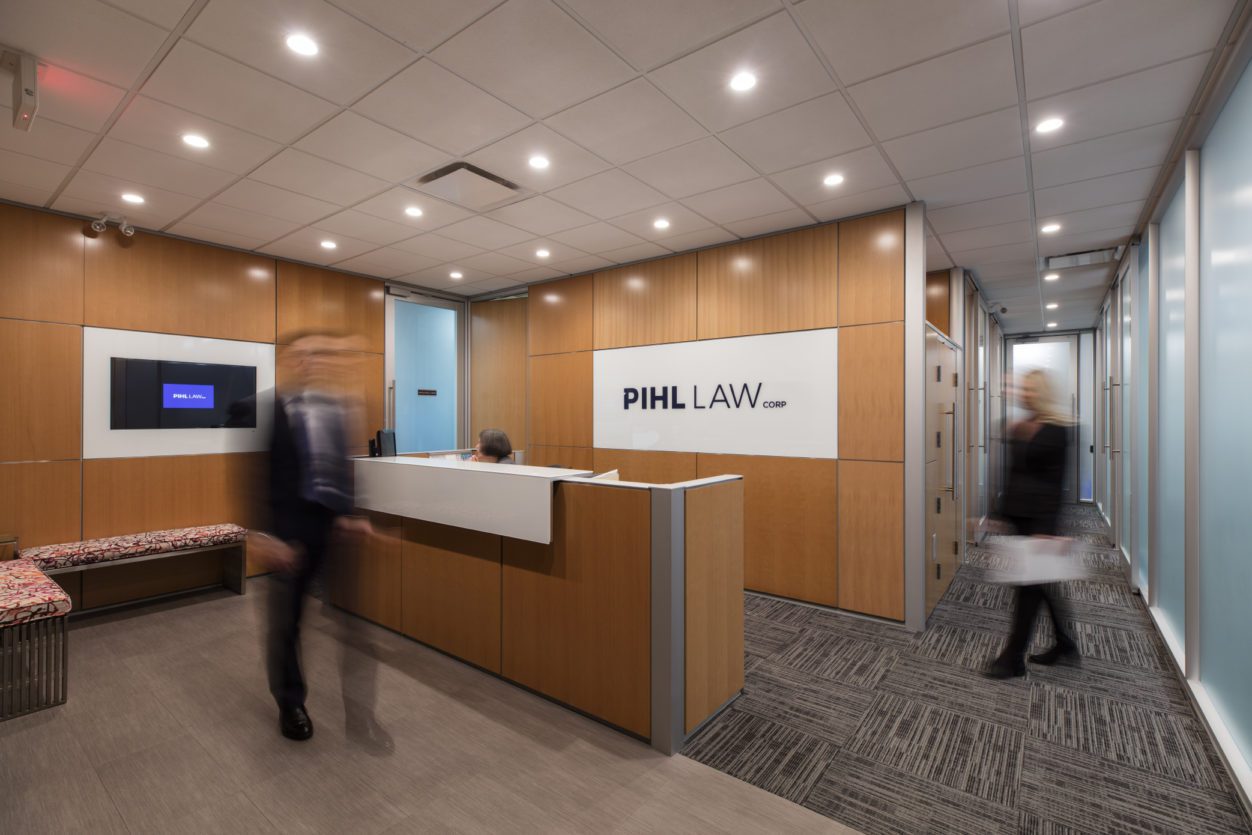 Pihl Law Office Reception with Employees Walking and Pihl Law logo on wooden background wall