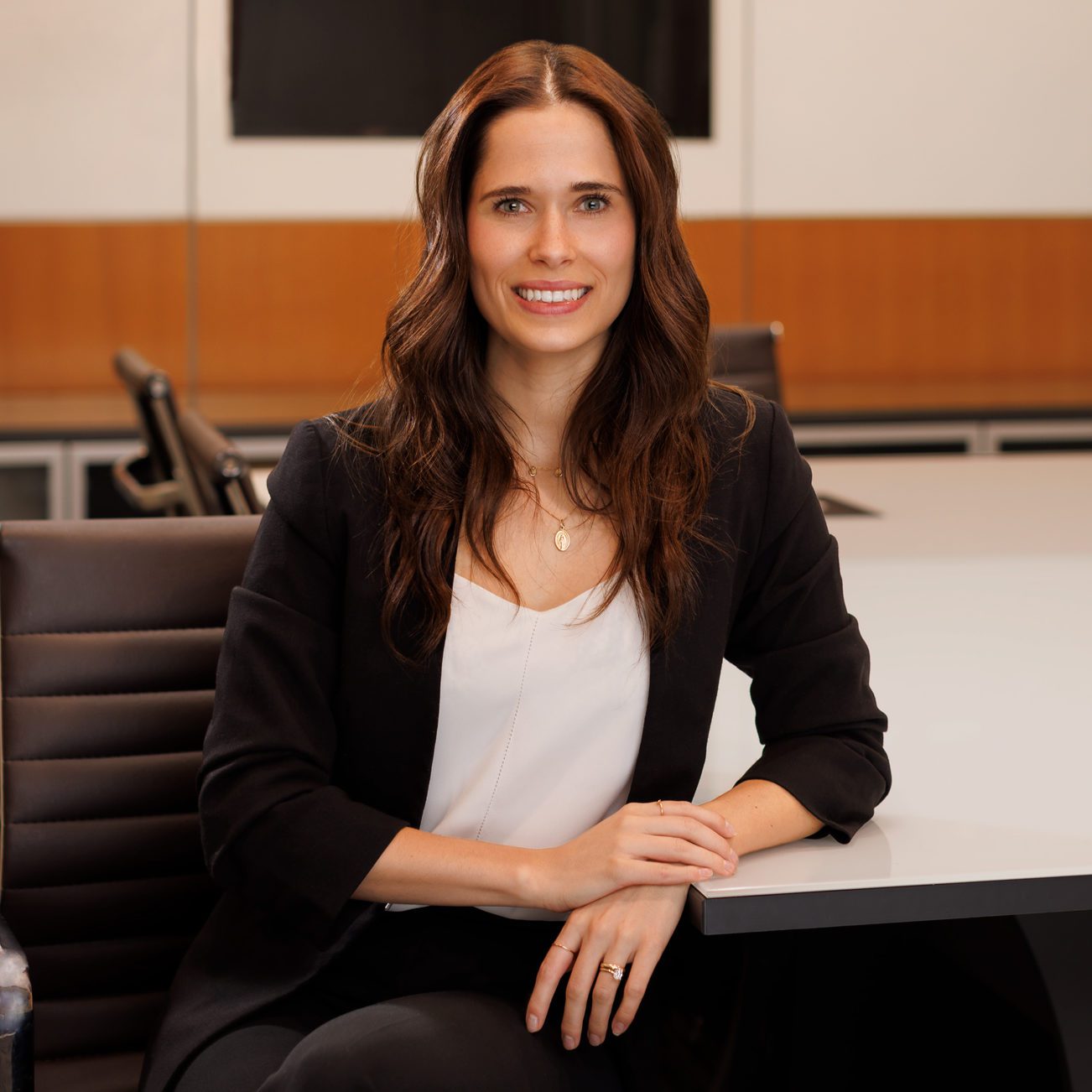 Megan Collins headshot wearing a black blazer and white shirt, against a white wall background