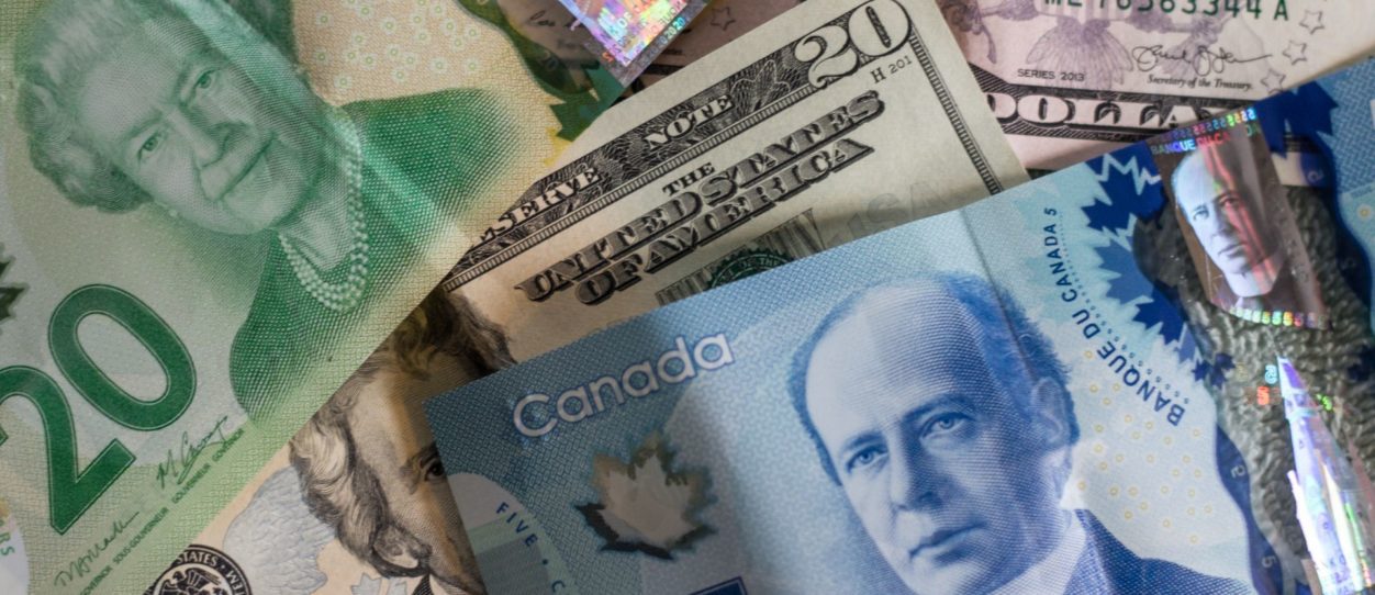 a closeup of money notes, including a blue canadian five dollar bill, a green twenty dollar canadian bill, and a twenty dollar american note
