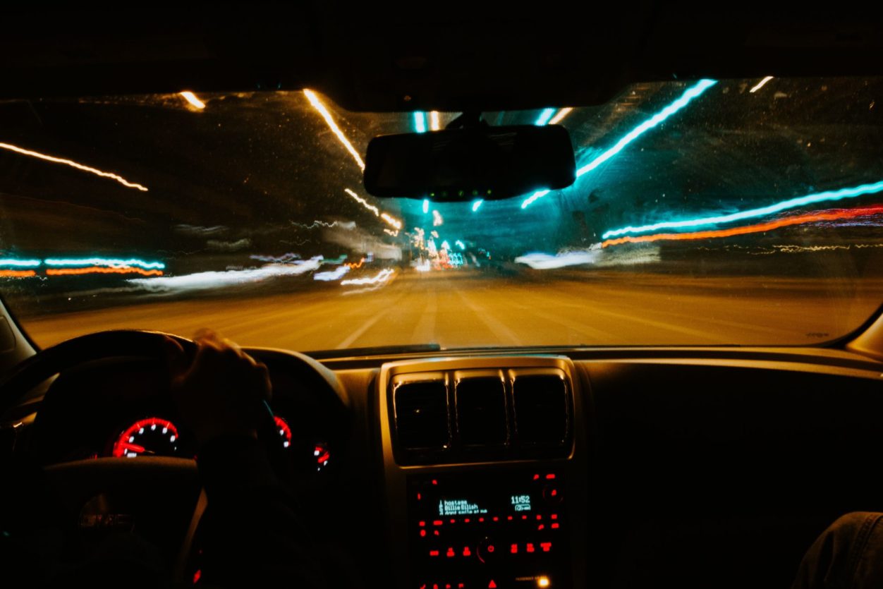 a car dashboard at night with lights on, looking out the front window at city lights passing by on a highway
