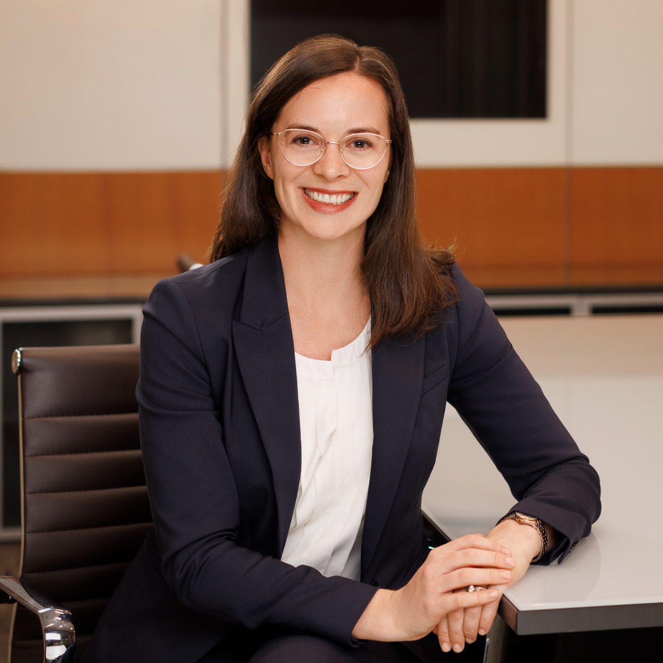 Rosie Jacobs, a brunette woman with glasses wearing a white shirt and blue blazer, sits at a table at Pihl Law.