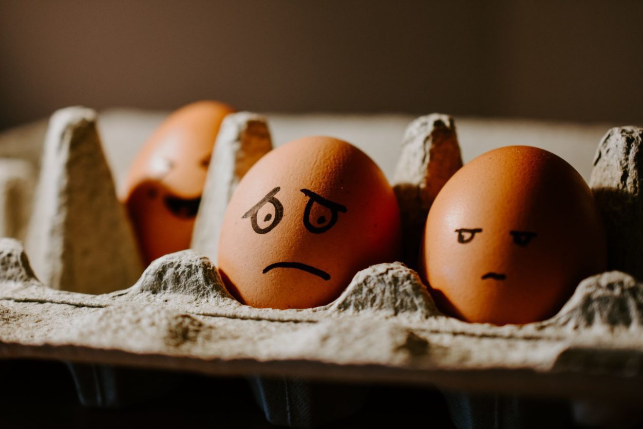 a closeup of two brown eggs in an egg carton with frown faces drawn in sharpie