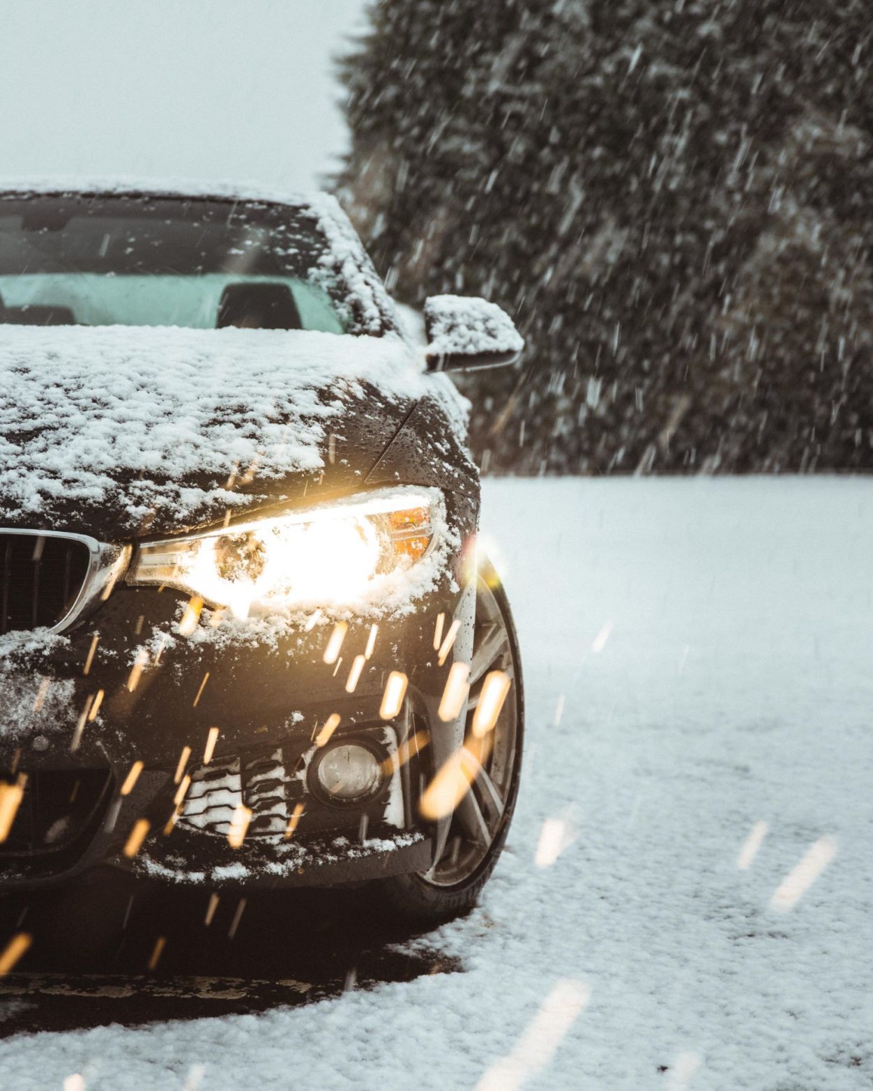 snow falling on a black car with lights on, highlighting winter driving
