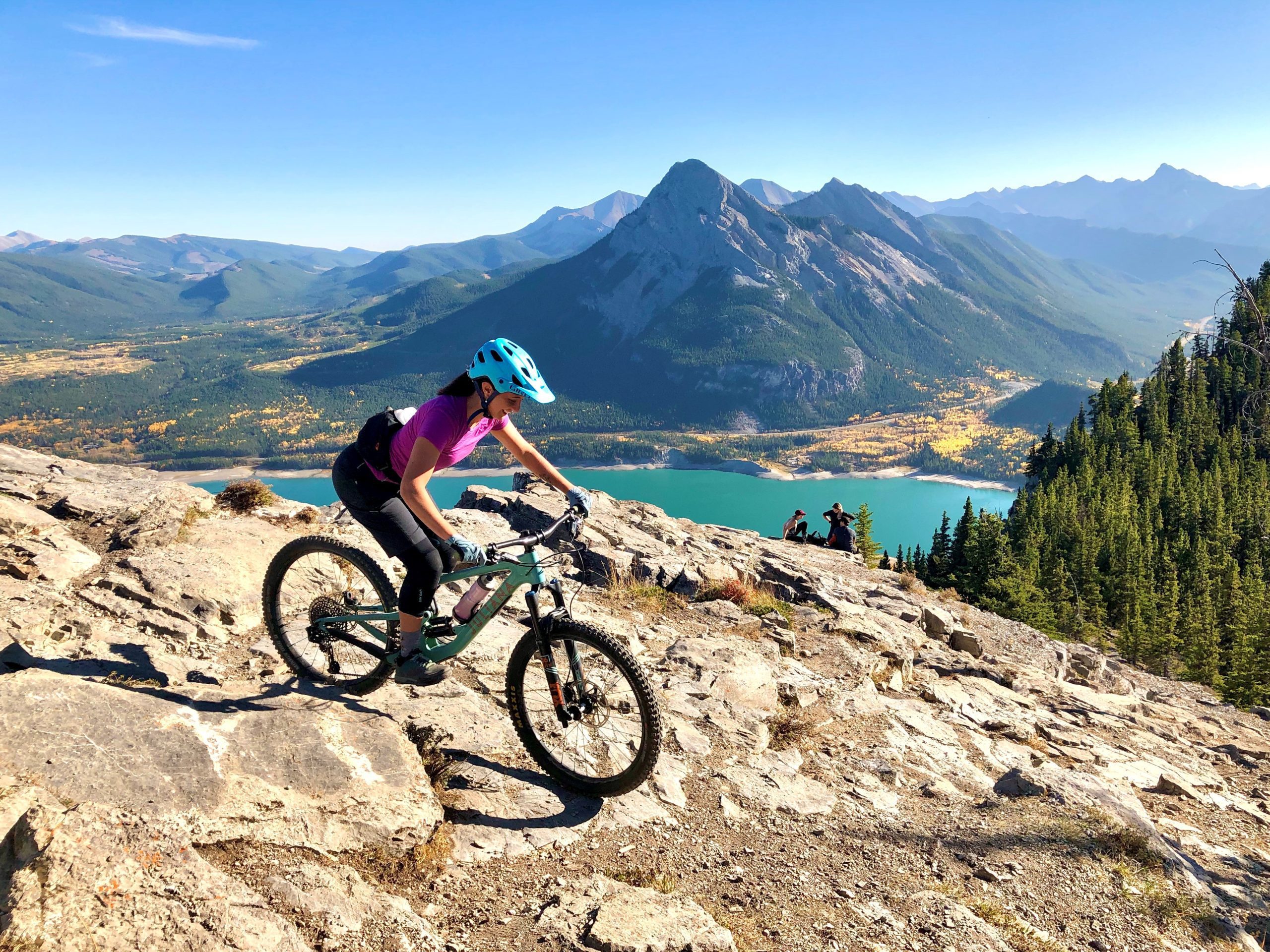 A woman mountain biking with a lake and mountain view in the background