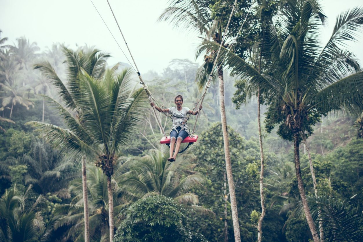 a woman sitting a wooden seat of a zipline suspended over a tropical forest